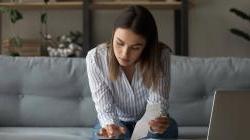 Young woman going over finances on couch at home with calculator, laptop, and receipts.